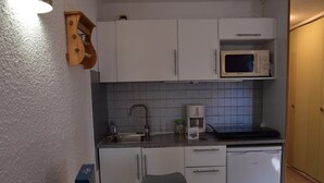 Eine kleine Küche mit weißen Schränken, einer Mikrowelle, einer Kaffeemaschine und einem Gesellschaftsspiel auf dem Tisch.