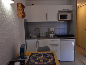 A compact kitchen with white cabinets, a microwave, a coffee maker, and a board game on the table. - Central studio in Montgenèvre - 2 guests (Montgenèvre)