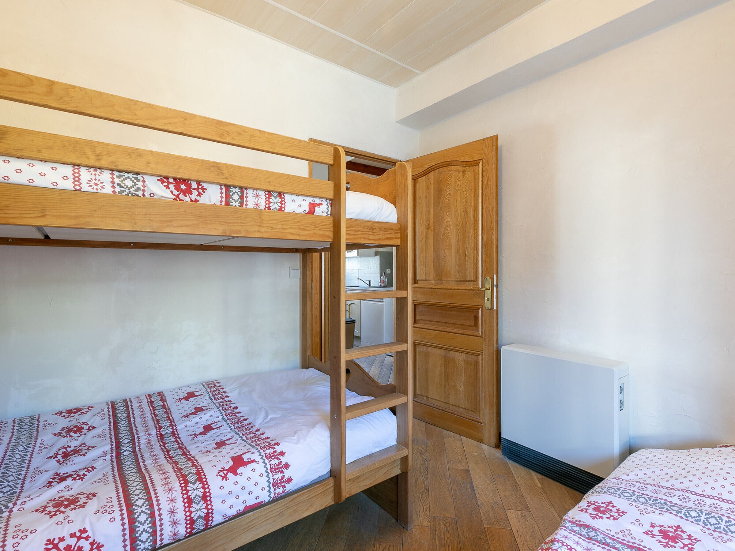 A bunk bed room with a wooden door, a radiator, and a small kitchenette.
