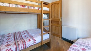 Habitación con literas, una puerta de madera, un radiador y una pequeña kitchenette.
