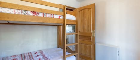 A bunk bed room with a wooden door, a radiator, and a small kitchenette.