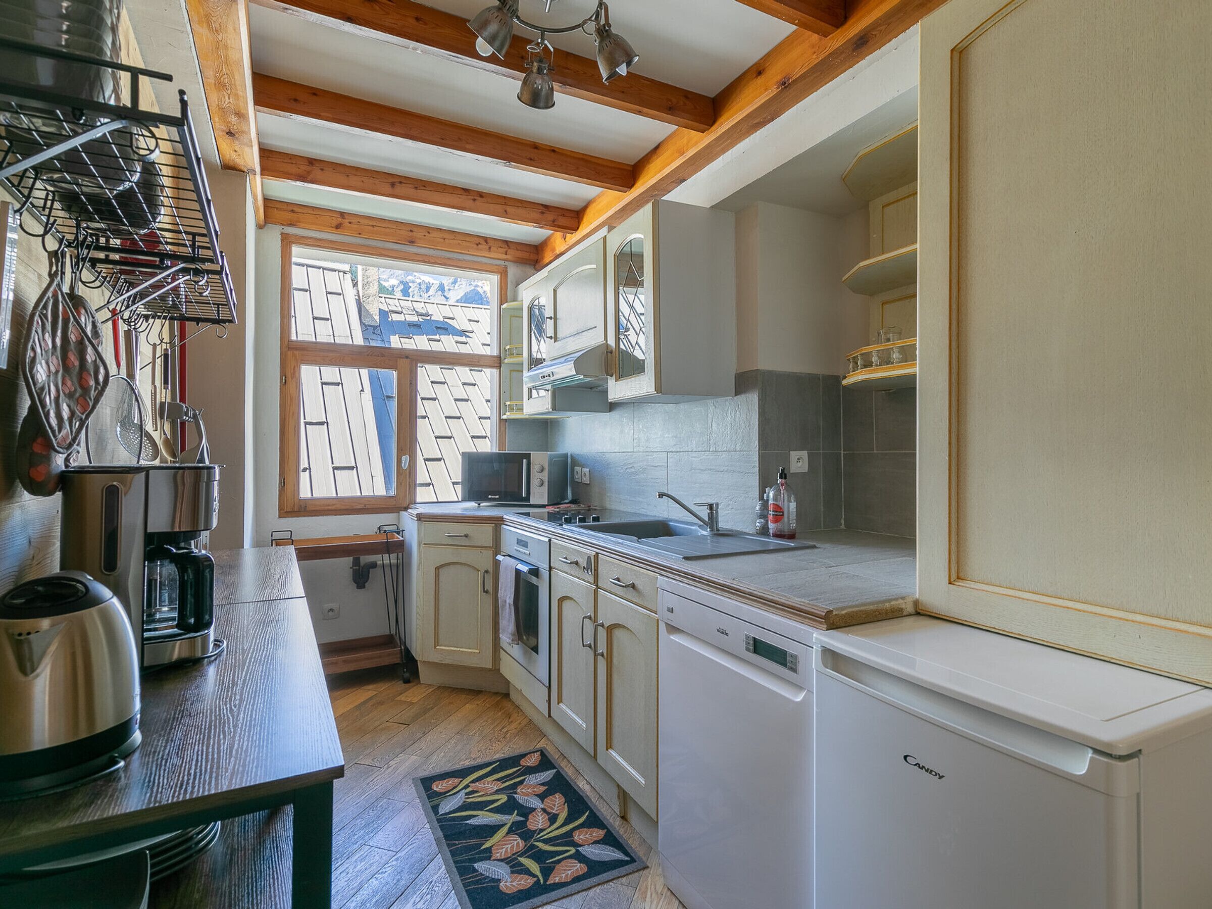 Cocina compacta con vigas de madera, un lavamanos, microondas y lavavajillas.