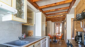 Una cocina con vigas de madera, un fregadero, una estufa y un comedor con sillas.