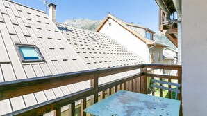 Un balcón con barandilla de madera, una mesa con estampado floral y vistas a una cordillera.