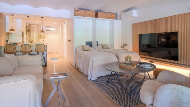 A modern living room with a sofa, a dining table, and a TV. There is a kitchen area with a counter and chairs. - Apartment sea view, AC - 4 guests (Platja d'Aro)