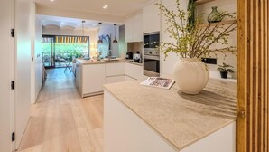 A modern kitchen with a central island, a dining area with a glass door leading outside, and a large vase with branches on the counter. - Apartment sea view, AC - 4 guests (Platja d'Aro)