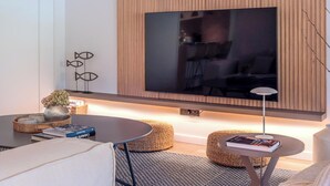 A modern living room with a flat-screen TV mounted on a wooden wall, a round coffee table, a small side table, and a sofa. - Apartment sea view, AC - 4 guests (Platja d'Aro)