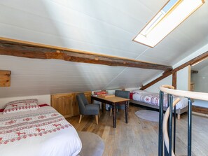 A cozy attic bedroom with a sloped ceiling, wooden beams, a small dining table, two chairs, a bed with patterned bedding, and a skylight. - Duplex apartment in village center - guests (Le Monêtier-les-Bains)