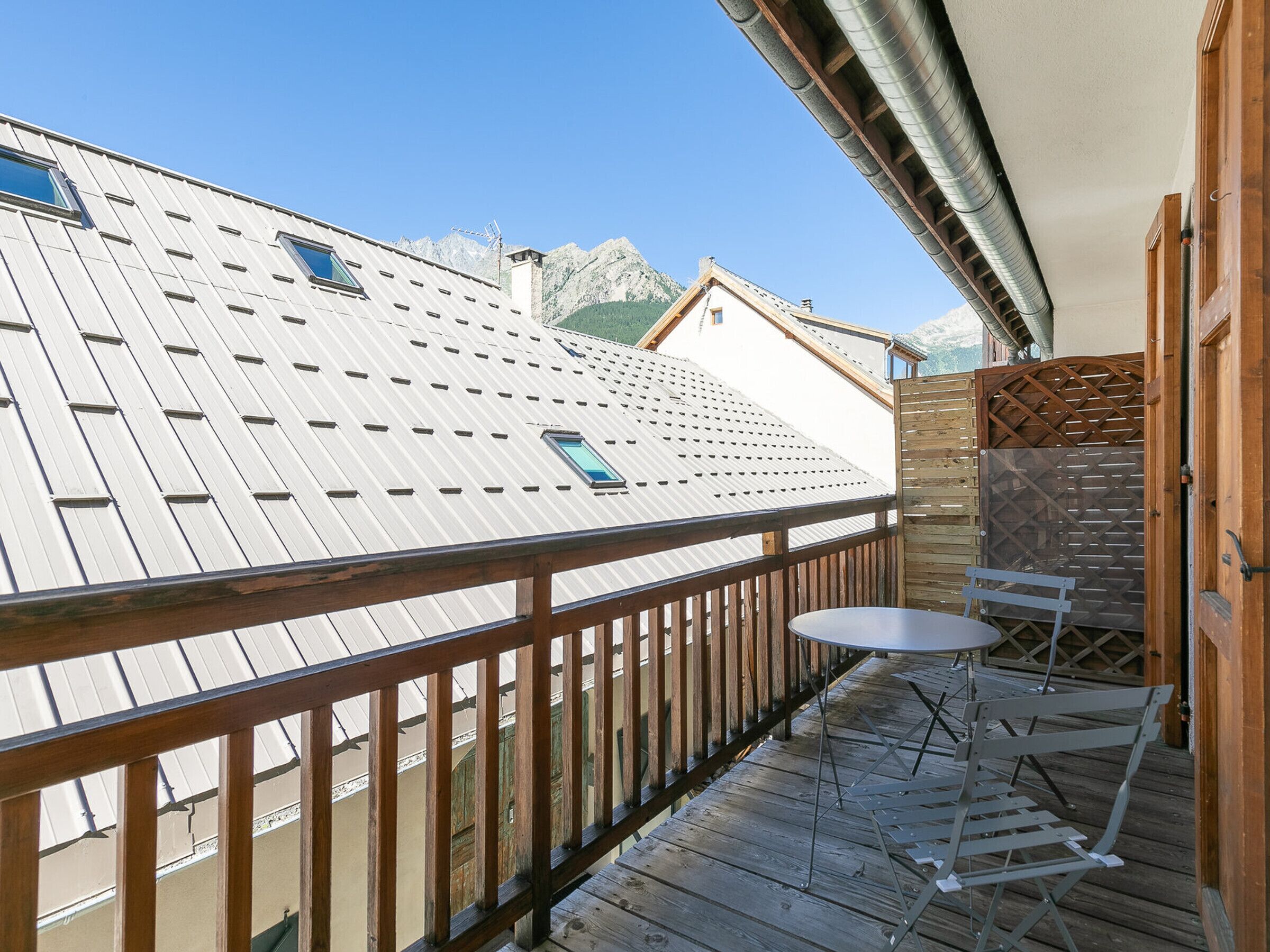 A wooden deck with a table and chairs, overlooking a mountain range.