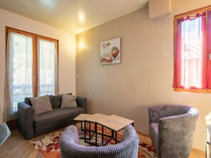 Ein Wohnzimmer mit einer Couch, einem kleinen Tisch, zwei Sesseln, einem Bild an der Wand und einem Fenster mit Vorhängen.