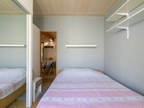 Ein Schlafzimmer mit zwei Betten, Holzboden, einem kleinen Tisch mit Stühlen und einer Tür zu einem anderen Raum.