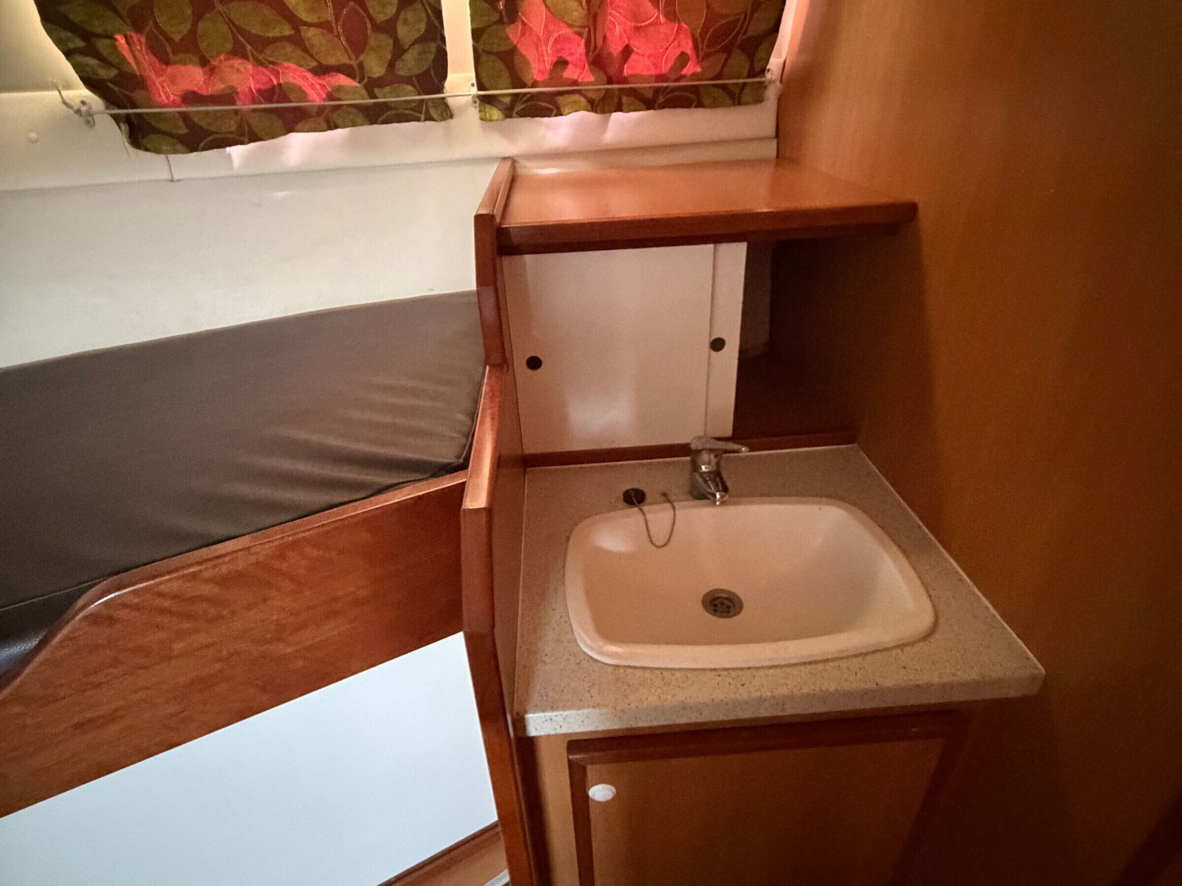 Une petite salle de bain avec un meuble-lavabo en bois, un évier et une fenêtre agrémentée de rideaux à motifs floraux.