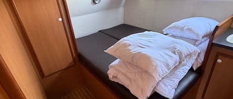A compact RV bedroom with a bed, a small window, and a door.