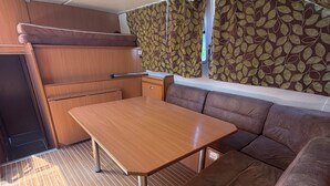 A compact RV interior with a wooden table, brown cushioned seating, and patterned curtains.