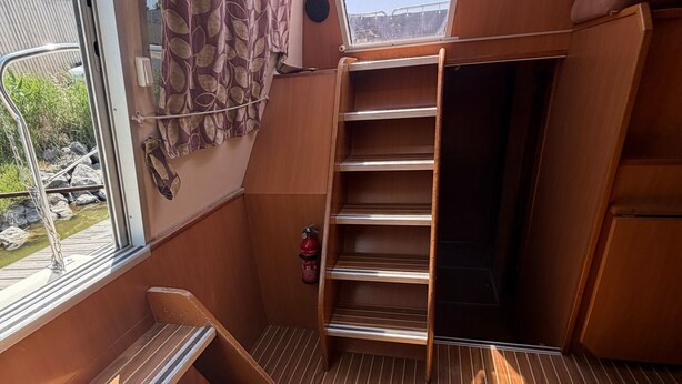 A compact, wooden interior with a built-in shelf unit and a window overlooking a garden.