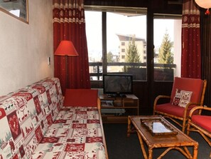 A cozy living room with a patterned sofa, a television, and two wicker chairs. - Central apartment, parking - 4 guests (Montgenèvre)
