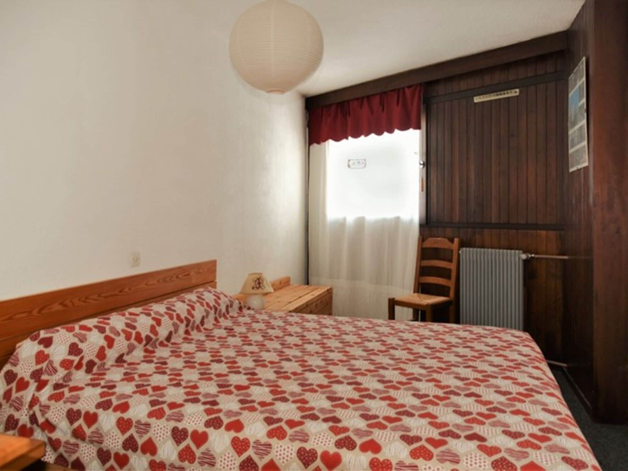 A bedroom with a bed, a nightstand, a chair, a radiator, and a window with curtains.