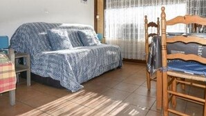 Ein Schlafzimmer mit einem Bett, das mit einer gemusterten Decke bezogen ist, einem Holzstuhl und einem kleinen Tisch.
