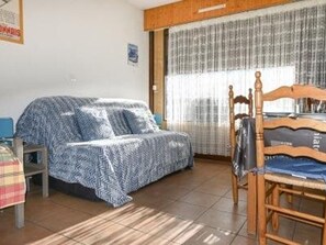 Ein Schlafzimmer mit einem Bett, das mit einer gemusterten Decke bezogen ist, einem Holzstuhl und einem kleinen Tisch.
