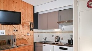 Eine kleine Küche mit Holzschränken, einer Mikrowelle, einem Spülbecken und einem Herd.