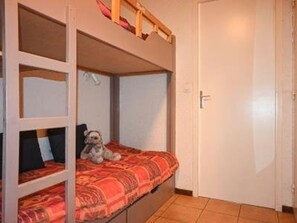 Ein Stockbett mit einem Hund auf der unteren Liege, einer Tür rechts und einem Fliesenboden.