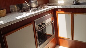Una cucina compatta con fornello a gas, bollitore, forno e lavello.