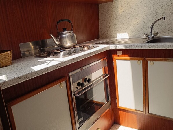 A compact kitchen with a gas stove, kettle, oven, and a sink.