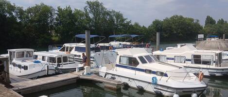 A marina with several boats docked, a wooden dock, and a calm water body surrounded by trees.