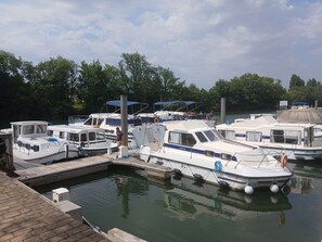 A marina with several boats docked, a wooden dock, and a calm water body surrounded by trees.