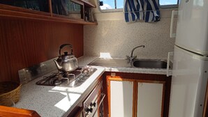 A compact kitchen with a gas stove, kettle, sink, and a refrigerator. - Discover our boat in Cognac - 7 to 9 guests (Cognac)
