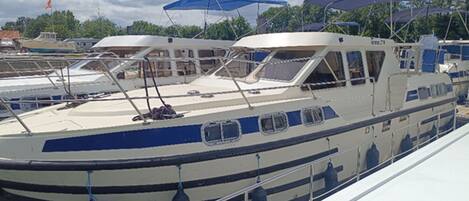 A boat docked at a marina with a covered deck area and a cabin structure.