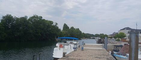 A paved dock with boats moored on the left, a clear sky, and a calm river.