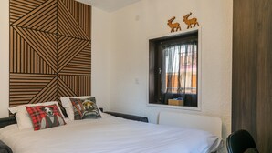 Ein Schlafzimmer mit einem Bett, Kissen, einem Fenster mit Vorhängen, einer Holzvertäfelung und einem kleinen Holzregal.