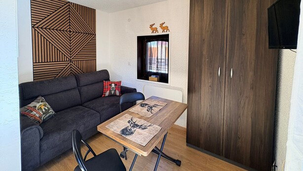 Ein modernes Wohnzimmer mit Sofa, Tisch mit Platzsets, einer Zierleiste an der Wand, einem Fenster mit Vorhängen und einem Kleiderschrank.