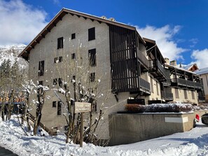 A multi-story building with a sloped roof, wooden balconies, and a sign in a foreign language. - Cozy studio in the heart of the station (Le Monêtier-les-Bains)