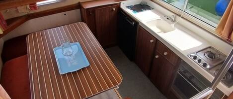 A compact kitchenette with a stove, sink, and a small dining area with a table and bench.