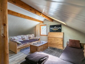 A cozy attic bedroom with a wooden ceiling, a sofa, a dresser, and a television displaying 'MOUNTAIN collection'.