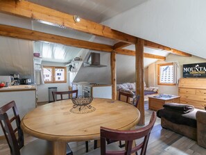 A cozy interior with a wooden dining table, chairs, a sofa, and a kitchen area with appliances.