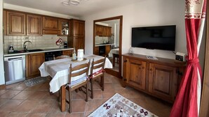 A compact kitchen with wooden cabinets, a dining table with chairs, a built-in oven, and a flat-screen TV mounted on the wall. - Apartment in central Montgenèvre - 4 guests (Montgenèvre)