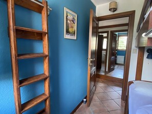 Un couloir avec une échelle en bois, une porte donnant sur une autre pièce et une affiche accrochée au mur.