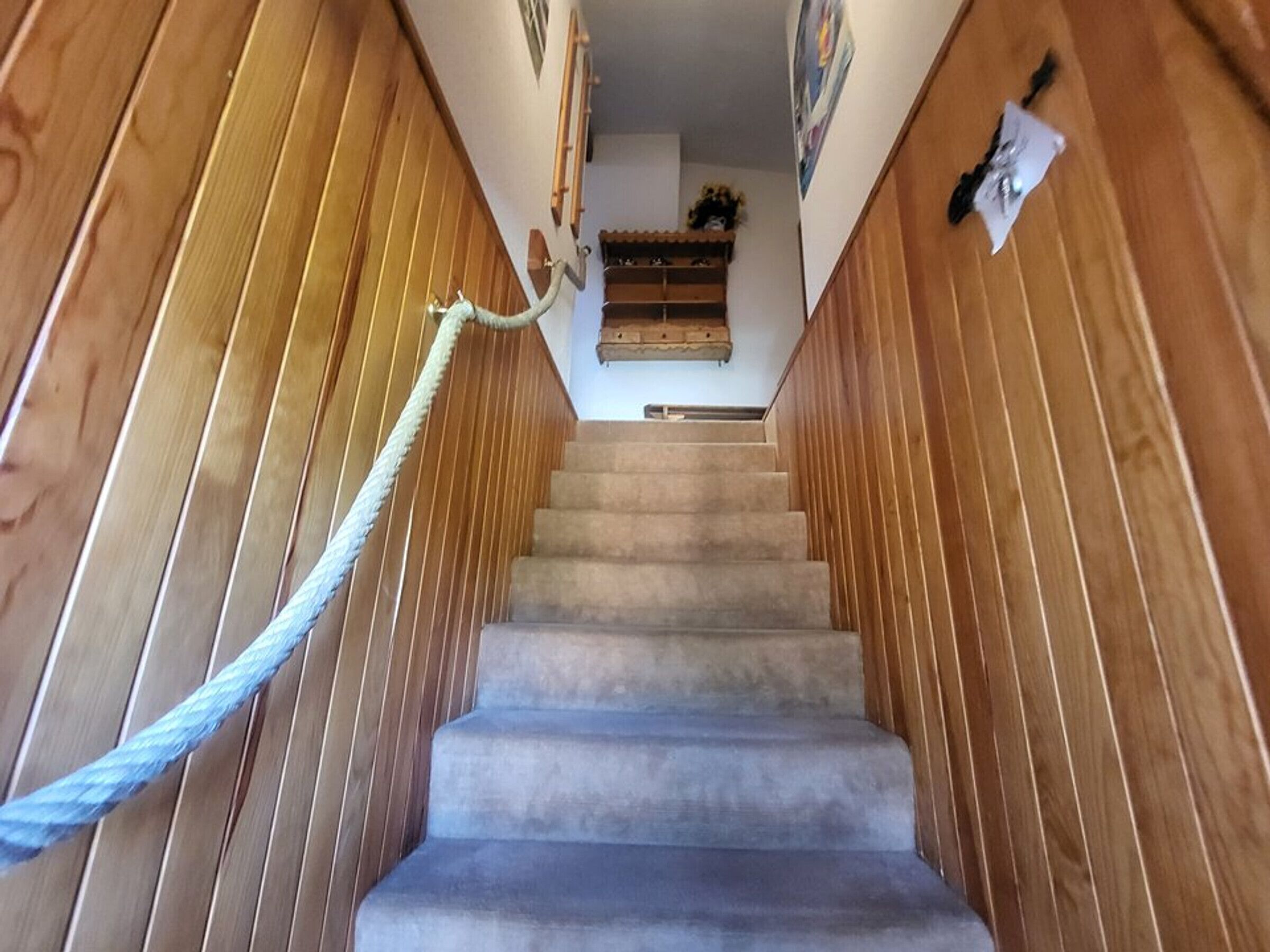 A wooden staircase with a rope handrail leading to a landing with a small shelf and a picture frame.