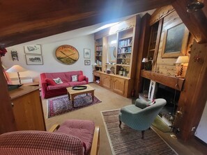 Ein gemütliches Wohnzimmer mit einem roten Sofa, einem blauen Sessel, einem Kamin und einem Holzregal.