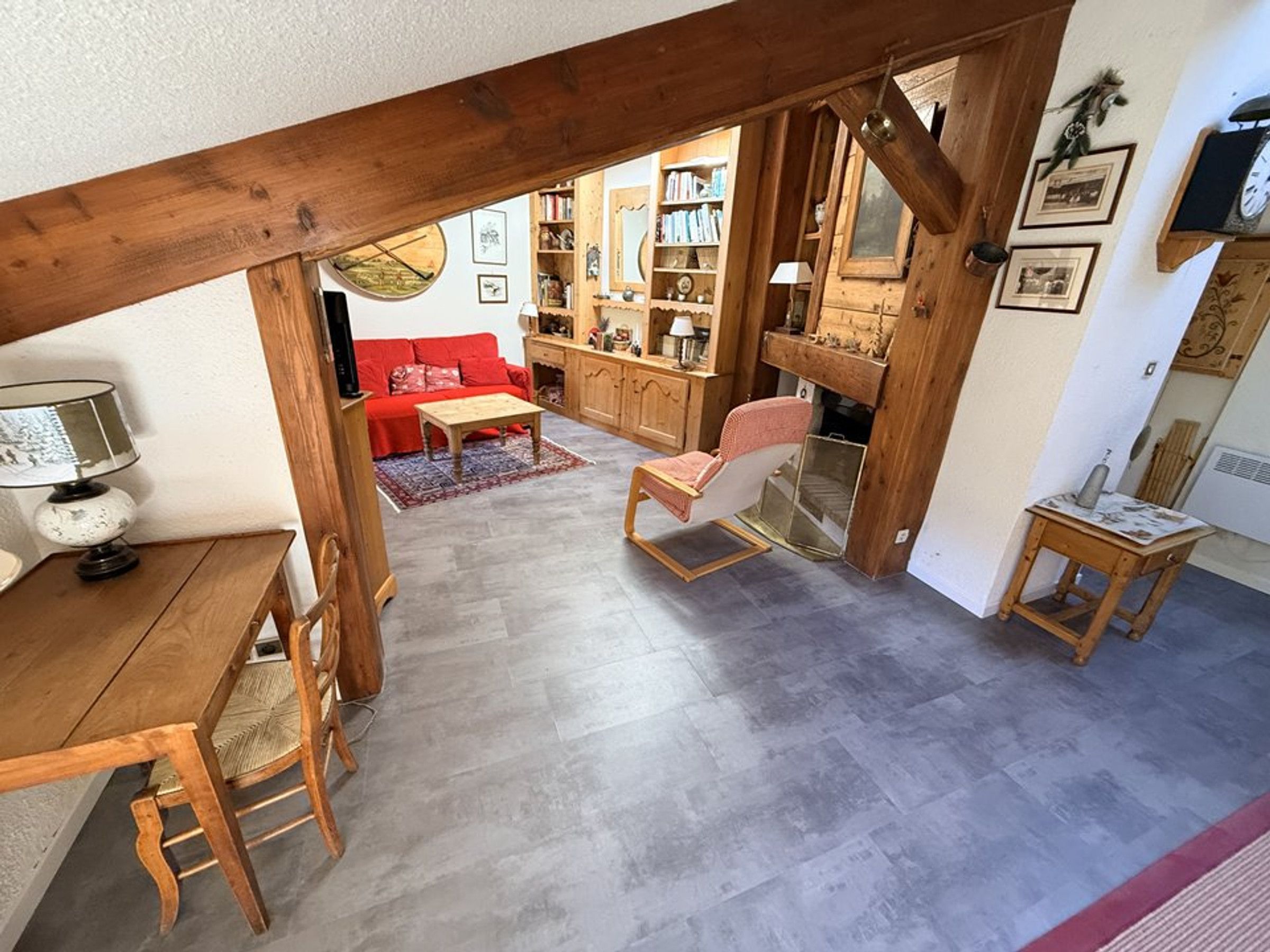A cozy living area with a wooden ceiling, a red sofa, a wooden dining table with chairs, and a small side table.