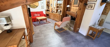 A cozy living area with a wooden ceiling, a red sofa, a wooden dining table with chairs, and a small side table.
