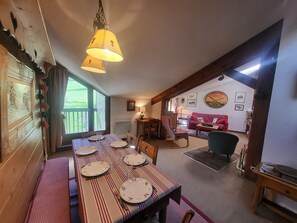 Ein Essbereich mit Tisch für vier Personen, eine rote Couch im Hintergrund und eine Holzbalkendecke.
