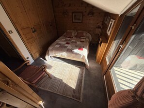 A cozy room with a bed, a chair, and a rug. - 3-bedroom apartment on the slopes - 6 guests (Montgenèvre)