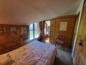 Ein Schlafzimmer mit Bett, Stuhl, Holzwänden, Fenster und Tür.