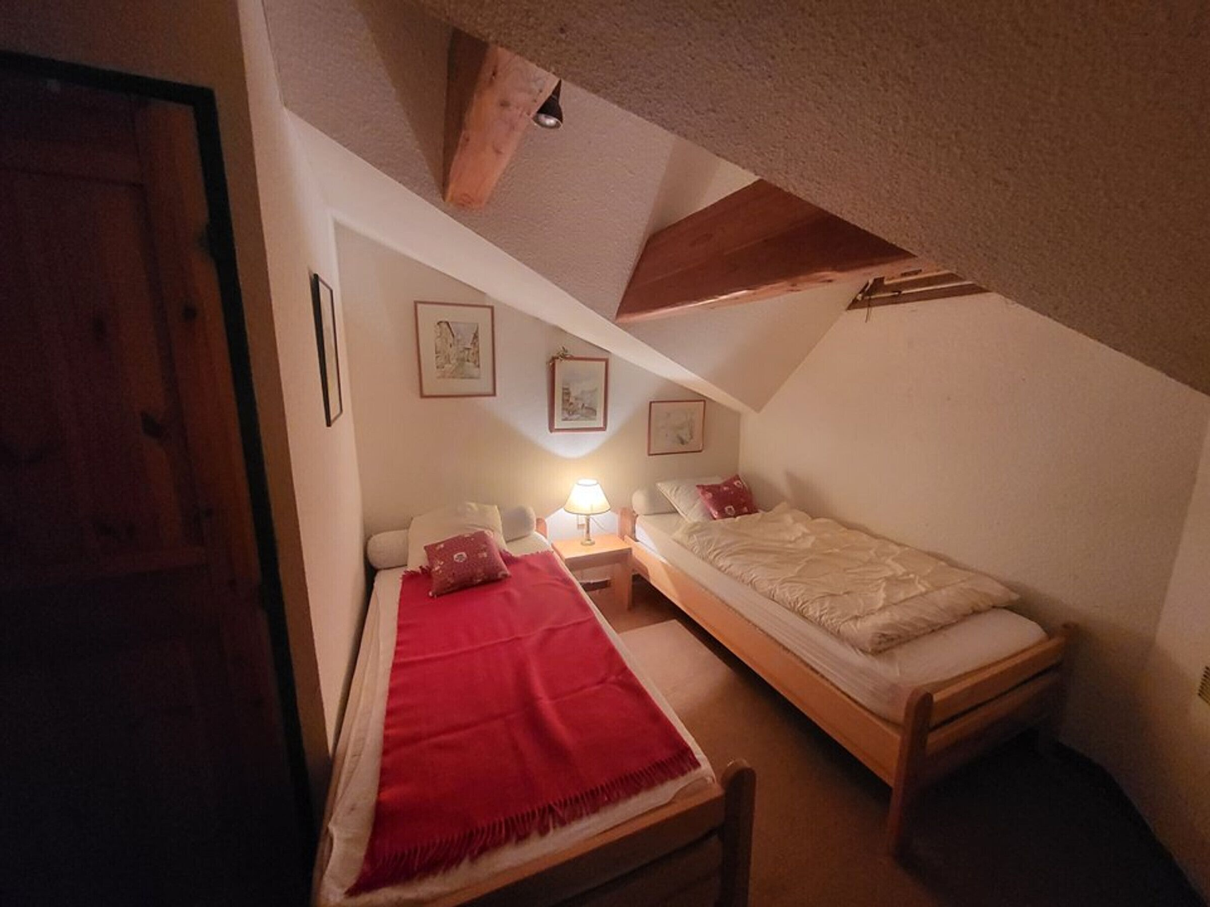 A small, cozy room with two beds, a wooden ceiling, and a door.