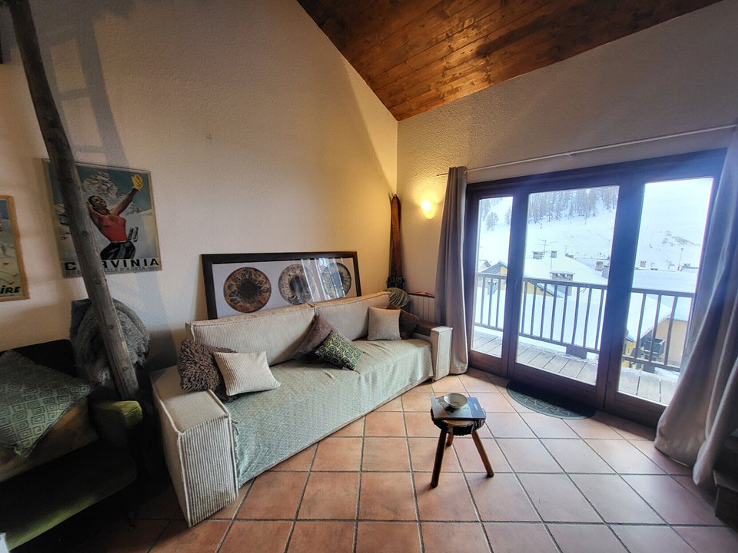 A cozy living room with a sofa, a small table, and a balcony with a view of a snowy landscape.