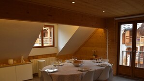 Un coin repas avec une table ronde dressée pour quatre personnes, des chaises blanches et une vue sur un bâtiment par la fenêtre.